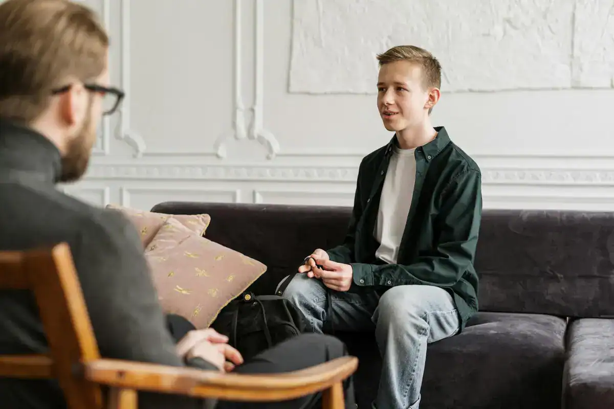 Teenage boy in therapy session with counselor at health and wellness clinic, mental health support, counseling, therapy session, teen mental health.