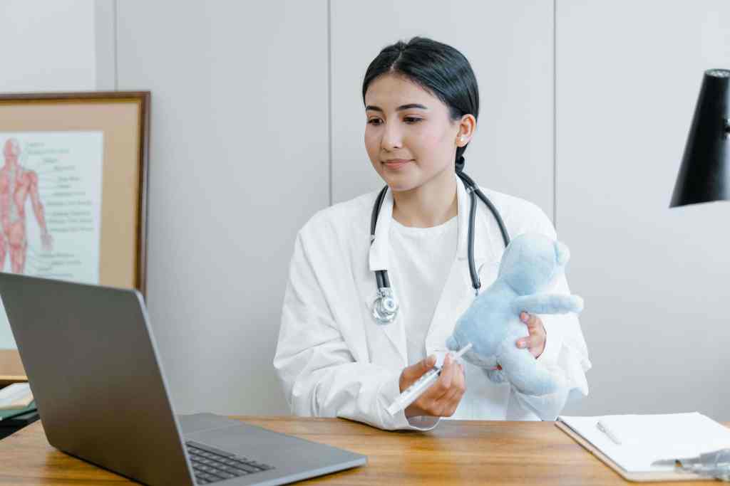 Young female doctor preparing a vaccine injection with a teddy bear in her office.